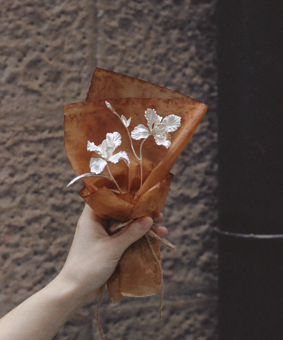 Hand holding a mini 925 sterling silver Iris Bouquet wrapped in rustic brown paper. Handmade Art Gifts by Lazesoul, blending delicate craftsmanship with timeless elegance for unique Iris Bouquet jewelry and keepsakes.