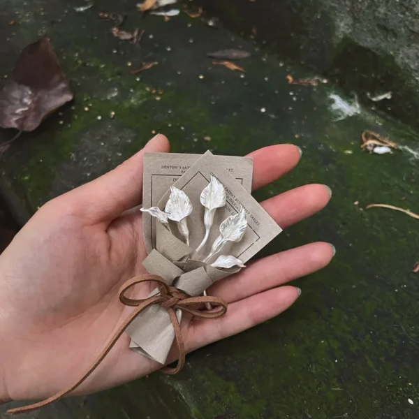Hand holding a delicate 925 sterling silver mini Calla Lily Bouquet, wrapped in rustic brown paper with string bow, Lazesoul Handmade Art Gifts, nature-inspired jewelry perfect for meaningful art gifts.