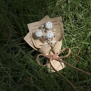 Handmade 925 sterling silver mini daisy bouquet brooch, presented as an elegant art gift. White floral design wrapped in rustic brown paper on green grass, perfect for nature-inspired jewelry lovers and Daisy Bouquet collectors.