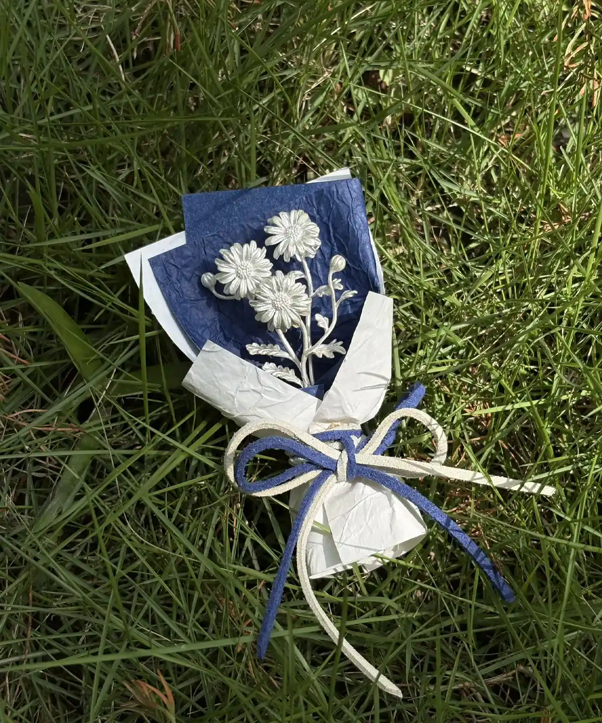 Handmade mini Daisy Bouquet art gift with delicate white flowers wrapped in crisp white paper and tied with a blue‑white bow, resting on lush green grass. Lazesoul 925 sterling silver inspired design, perfect for décor, photography, and gifting.