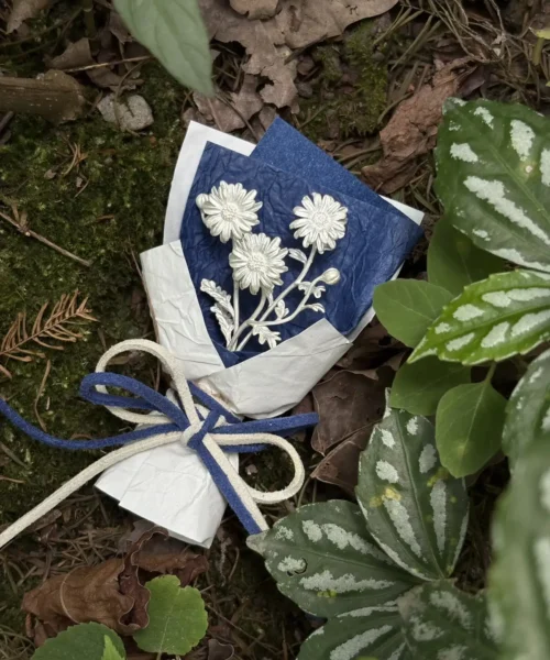 Handmade 925 sterling silver mini daisy bouquet displayed in a natural woodland setting, wrapped in textured white paper with a blue floral card. Unique Lazesoul art gifts blending nature-inspired beauty with timeless craftsmanship.