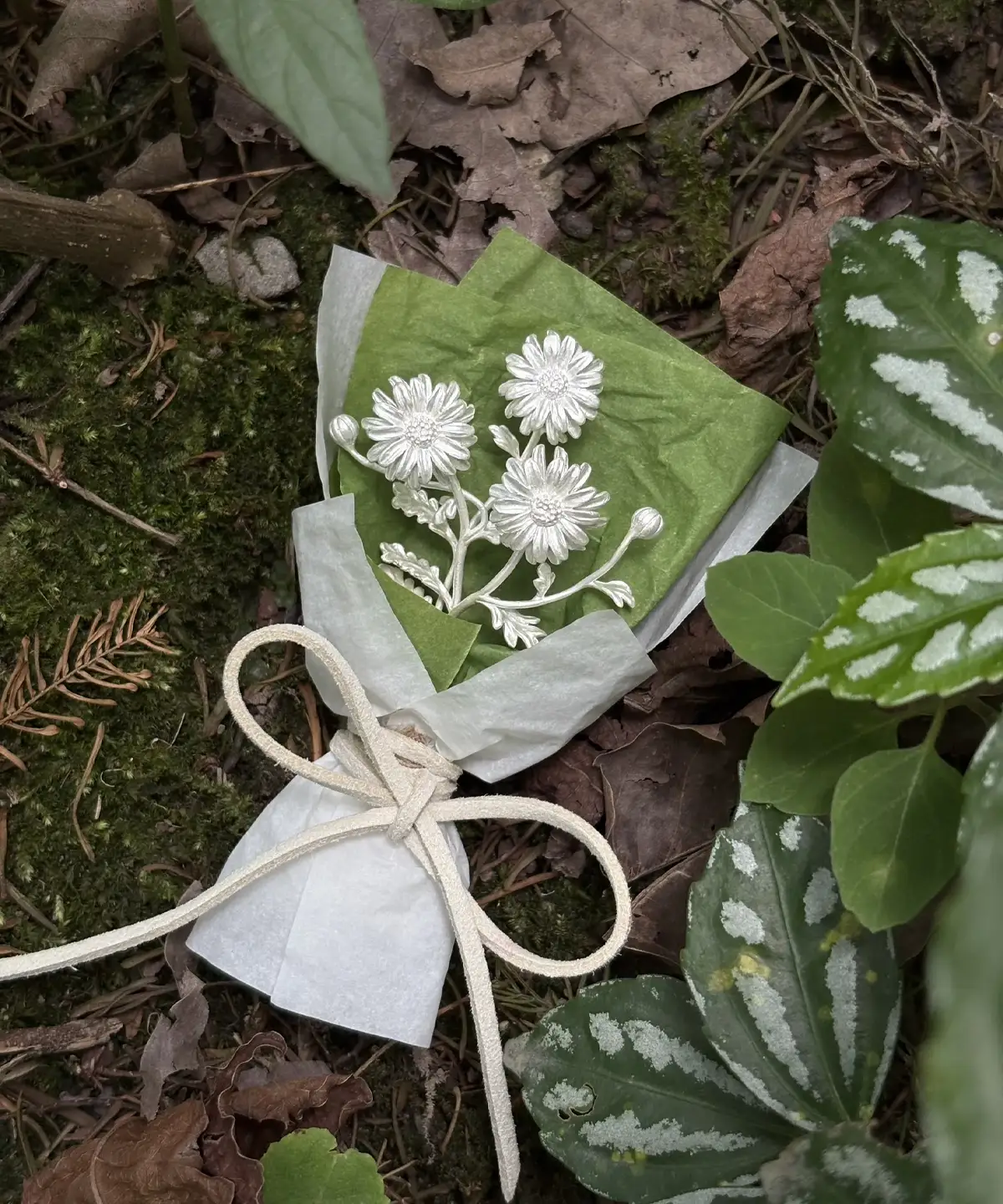 A nature‑inspired display of the 925 sterling silver mini daisy bouquet from Lazesoul Handmade Art Gifts, styled with moss, leaves, and twine wrapping, evoking artisanal charm and timeless beauty in this delicate Daisy Bouquet art gift.