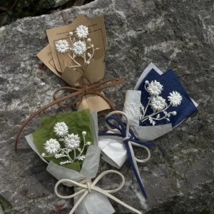 Handcrafted mini daisy bouquet with white daisies and baby’s breath, wrapped in green, brown, and blue paper. Perfect as handmade art gifts, this 925 sterling silver inspired daisy bouquet adds charm to home décor or special occasions.
