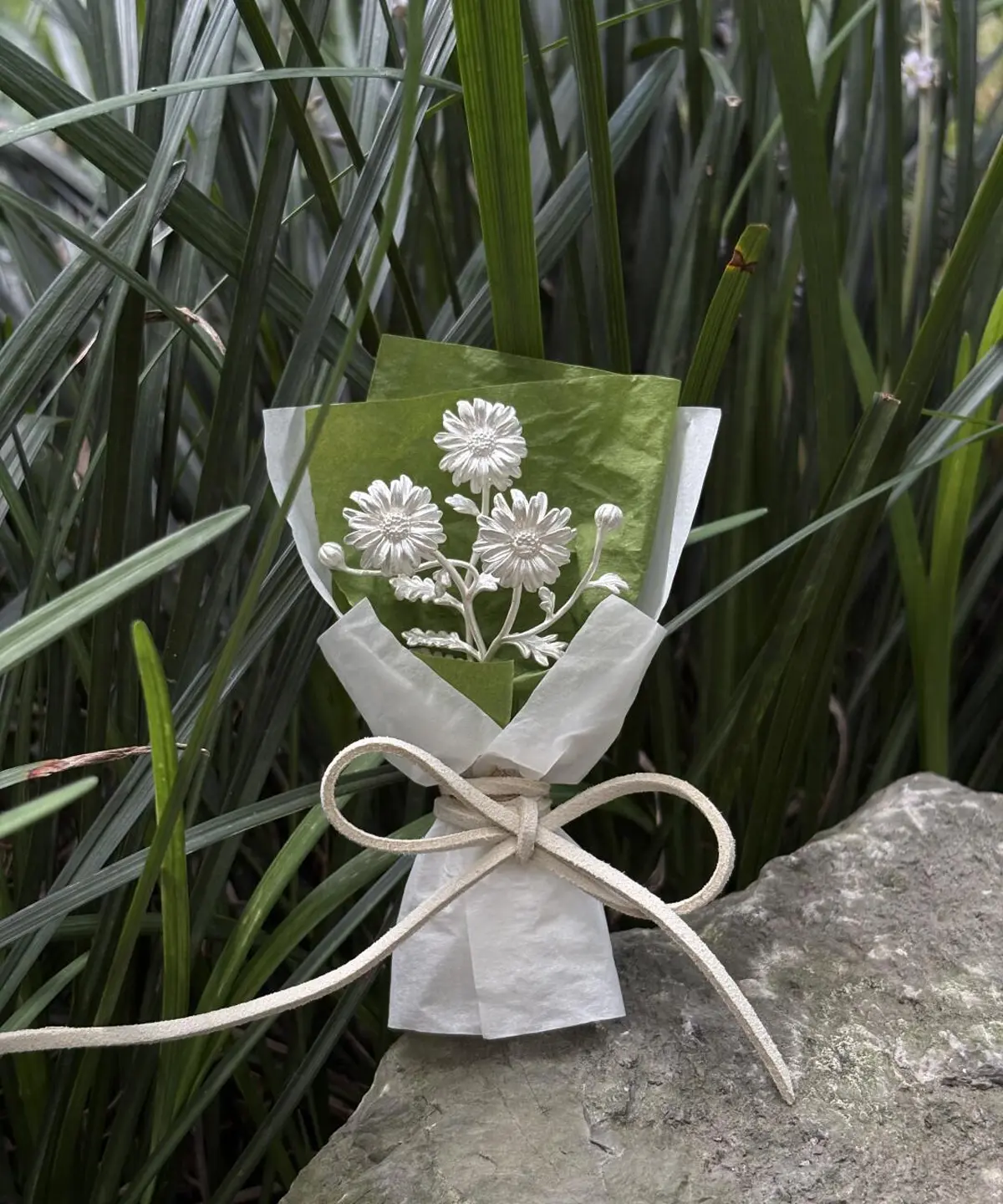 Handmade 925 sterling silver mini daisy bouquet displayed on a rock with green grass background. Elegant white petals and lifelike details make this Daisy Bouquet a perfect choice for nature-inspired art gifts and timeless keepsakes.