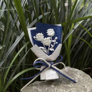 Handmade 925 sterling silver mini daisy bouquet displayed on a rock with green grass backdrop. Elegant white daisies on deep blue paper, wrapped with dual‑color bow. Perfect daisy bouquet for unique handmade art gifts by Lazesoul.