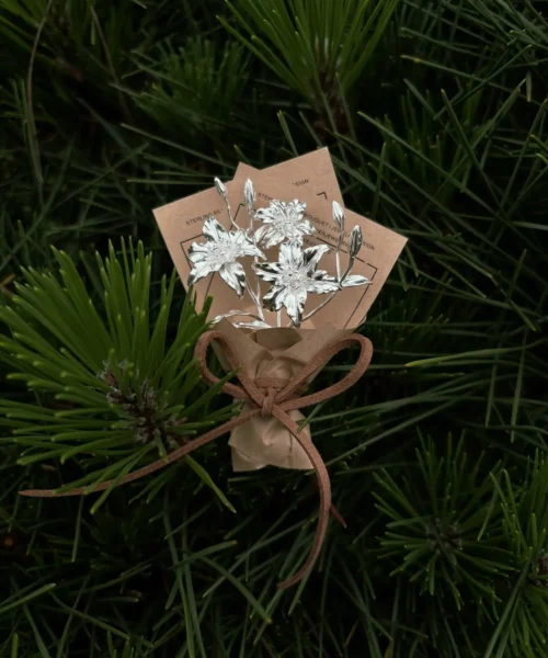 A handcrafted 925 sterling silver mini Lily Bouquet displayed with vintage paper accents and pine backdrop, perfect as unique handmade art gifts. Elegant design blends nature-inspired beauty with timeless artisanal charm.