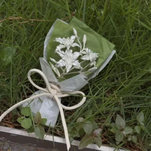 A 925 sterling silver mini lily bouquet wrapped in green and white tissue with a beige bow, handmade by Lazesoul. Elegant metallic lilies on natural grass, perfect as unique art gifts for special occasions or decorative keepsakes.