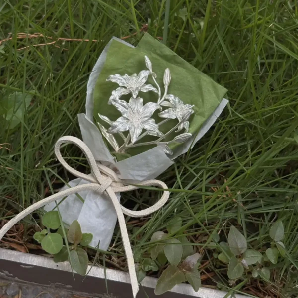 925 Sterling Silver Mini Lily Bouquet-Handmade Art Gifts 04 A 925 sterling silver mini lily bouquet wrapped in green and white tissue with a beige bow, handmade by Lazesoul. Elegant metallic lilies on natural grass, perfect as unique art gifts for special occasions or decorative keepsakes.