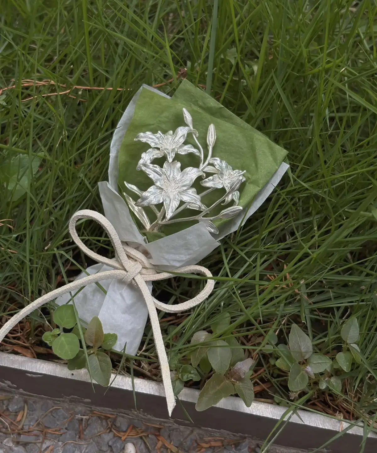 A 925 sterling silver mini lily bouquet wrapped in green and white tissue with a beige bow, handmade by Lazesoul. Elegant metallic lilies on natural grass, perfect as unique art gifts for special occasions or decorative keepsakes.
