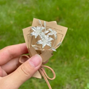 Hand holding a 925 sterling silver mini lily bouquet wrapped in kraft paper with suede string, Lazesoul handmade art gifts. Elegant resin flowers with cards, perfect Lily Bouquet for unique art gifts and timeless keepsakes.