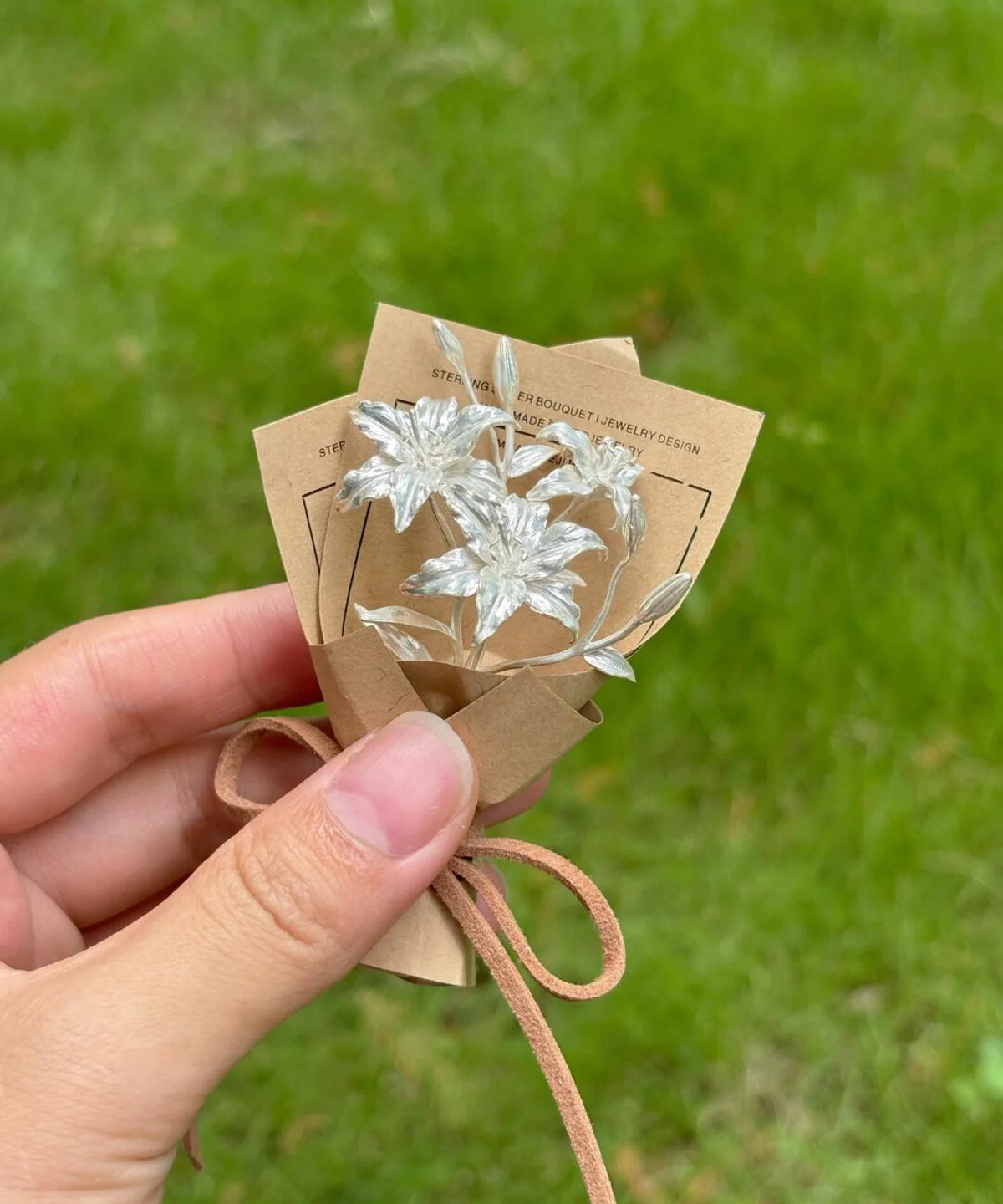 Hand holding a 925 sterling silver mini lily bouquet wrapped in kraft paper with suede string, Lazesoul handmade art gifts. Elegant resin flowers with cards, perfect Lily Bouquet for unique art gifts and timeless keepsakes.