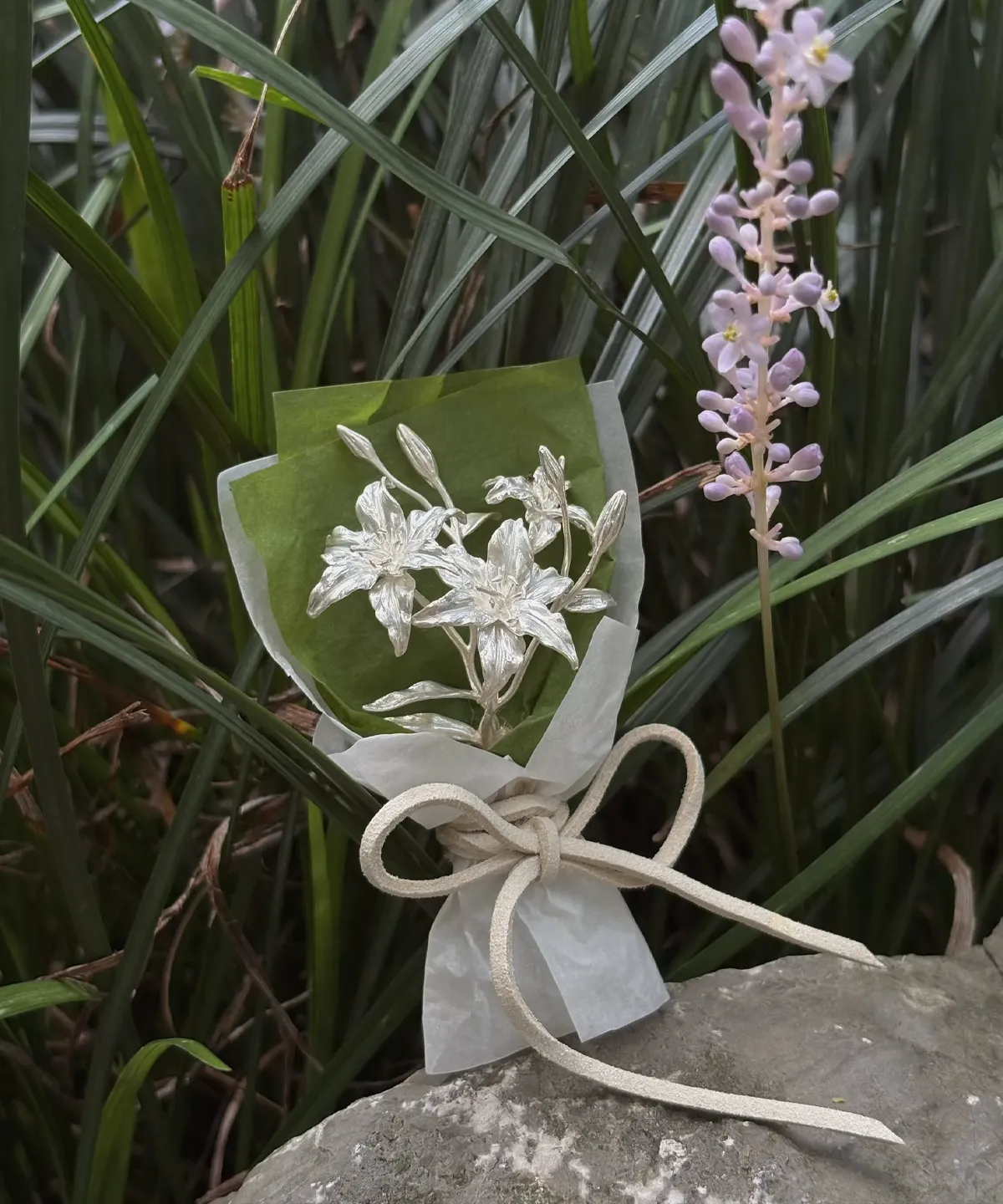 925 Sterling Silver Mini Lily Bouquet resting on a rock beside lavender blooms, wrapped in green and white paper with ribbon — Lazesoul Handmade Art Gifts, perfect for elegant keepsakes and nature‑inspired décor.