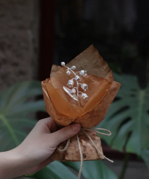 Hand holding a rustic-wrapped mini Lily Of The Valley Bouquet with delicate white bell flowers, inspired by Lazesoul Handmade Art Gifts. 925 sterling silver design, perfect for nature lovers and unique art gifts collectors.