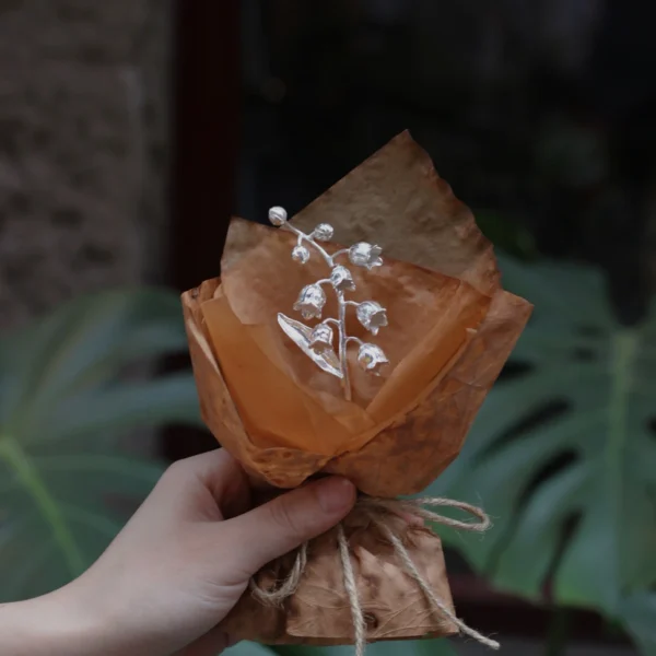 Hand holding a rustic-wrapped mini Lily Of The Valley Bouquet with delicate white bell flowers, inspired by Lazesoul Handmade Art Gifts. 925 sterling silver design, perfect for nature lovers and unique art gifts collectors.