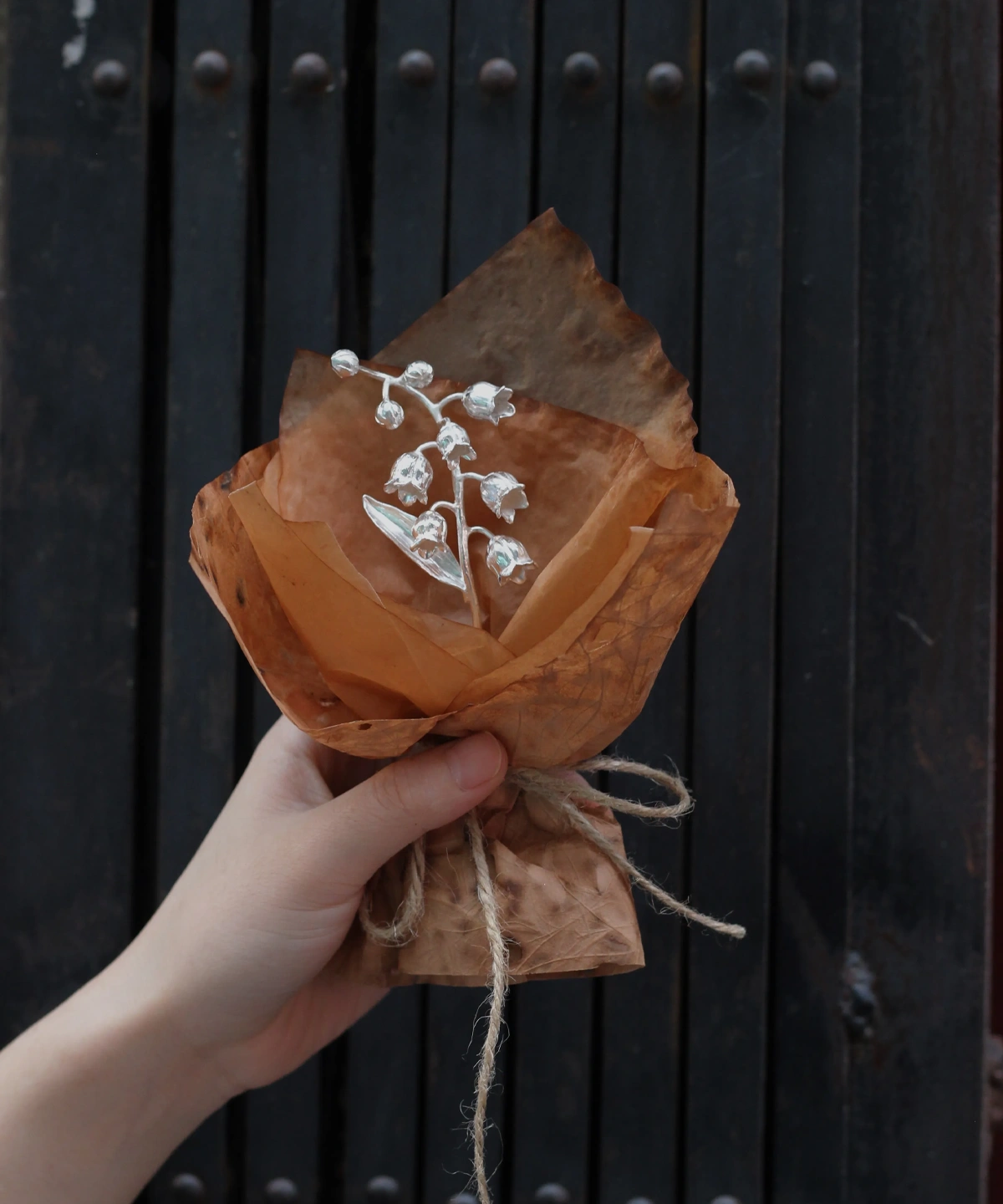 Hand holding a rustic-wrapped Lily of the Valley Bouquet, inspired by Lazesoul Handmade Art Gifts. Features delicate white bell-shaped flowers, evoking elegance and nature in 925 sterling silver jewelry design.