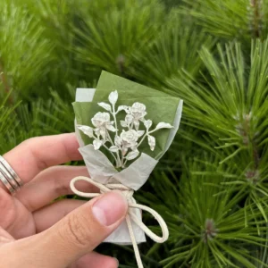 Hand holding a 925 sterling silver mini rose bouquet wrapped in green and white paper with a beige bow, Lazesoul handmade art gifts, nature-inspired jewelry and decorative keepsake, perfect rose bouquet for unique art gifts lovers.
