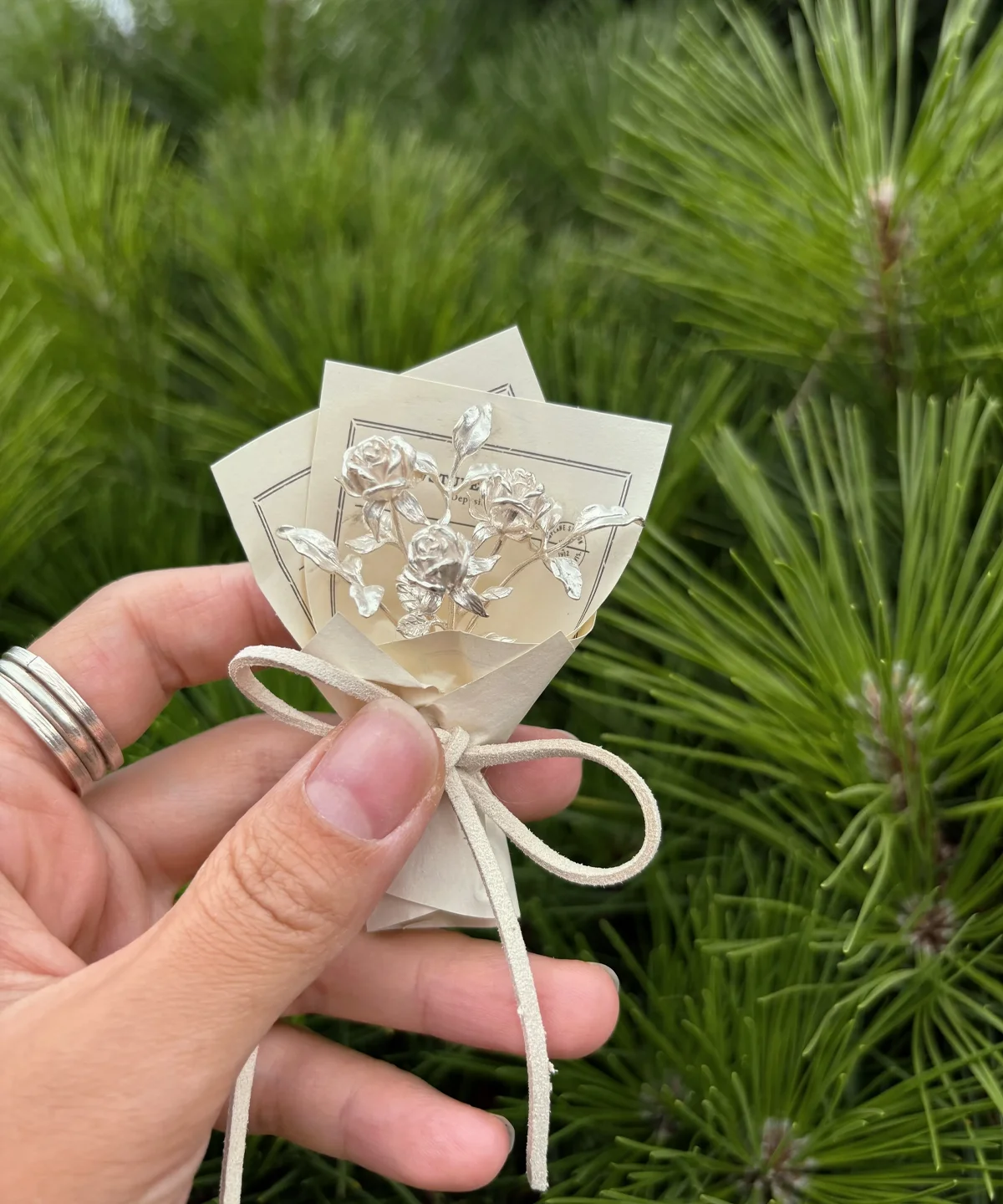 Hand holding a 925 sterling silver mini rose bouquet wrapped in paper with string bow, Lazesoul handmade art gifts, nature-inspired design, perfect rose bouquet keepsake for unique art gifts lovers.