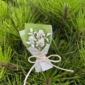 A delicate 925 sterling silver mini rose bouquet, handcrafted with intricate detail, wrapped in green and white paper, resting on pine needles. Perfect handmade art gifts for nature lovers and collectors of unique rose bouquet designs.