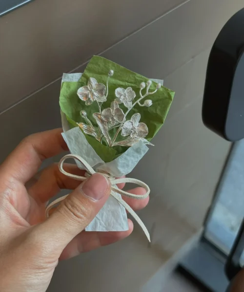 A delicate 925 sterling silver Phalaenopsis mini bouquet, handmade with intricate metallic flowers and leaves, wrapped in white and green paper with a ribbon. Perfect for Lazesoul art gifts, blending elegance and craftsmanship.