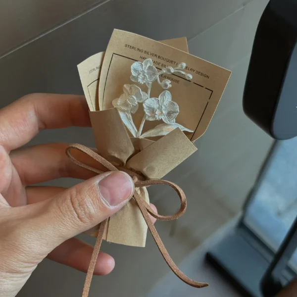 A delicate 925 sterling silver Phalaenopsis Mini Bouquet presented in brown paper with ribbon, blending floral artistry and fine jewelry. Perfect for Lazesoul Handmade Art Gifts, ideal for unique keepsakes and elegant gift-giving.