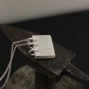 Close-up of Lazesoul Love Letter 925 sterling silver personalized book necklace, handmade with miniature notebook pendant engraved “Love letter About Us,” on silver chain. Elegant custom jewelry gift for her.
