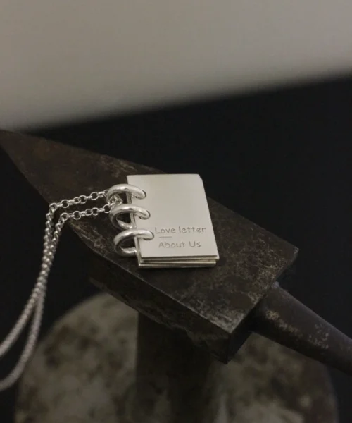 Close-up of Lazesoul Love Letter 925 sterling silver personalized book necklace, handmade with miniature notebook pendant engraved “Love letter About Us,” on silver chain. Elegant custom jewelry gift for her.