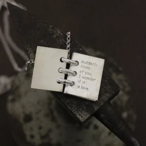 Close-up of Lazesoul Love Letter 925 sterling silver personalized book necklace, handmade with open notebook pendant engraved “suddenly think of you, I wonder if it is love,” on silver chain. Elegant custom jewelry gift.