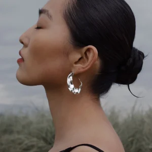 Close-up side profile of a woman wearing Lazesoul’s Moon Aria 990 pure silver sculptural Moon Earrings, set against a serene natural landscape with tall grass and cloudy sky, highlighting the handmade artistry and elegant lunar-inspired design.