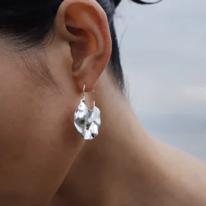 Close-up of Lazesoul’s Moon Aria 990 pure silver sculptural Moon Earrings, handmade with an abstract, organic design. The reflective silver curves catch the light, evoking moonlit elegance against a soft, cloudy sky backdrop.