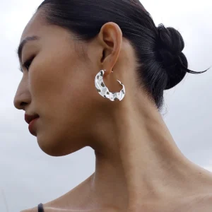 Side profile of a woman wearing Lazesoul’s Moon Aria 990 pure silver sculptural moon earrings, handmade art jewelry with a bold abstract hoop design, set against a soft cloudy sky for a modern, elegant look.