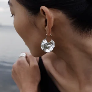 Close-up of Lazesoul Moon Aria 990 pure silver sculptural Moon Earrings, handmade with an organic, crumpled texture. Worn outdoors by the water, the artisanal design reflects moonlit elegance and contemporary art jewelry craftsmanship.