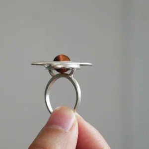Hand holding Lazesoul’s handmade Saturn Ring in 925 sterling silver, featuring a polished tiger’s eye gemstone as Saturn with sculptural orbit bands; celestial-inspired artisan jewelry blending cosmic symbolism with modern elegance.