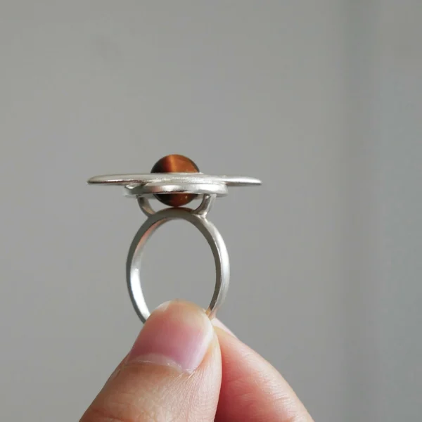 925 Sterling Silver Tiger’s Eye Saturn Ring 01 Hand holding Lazesoul’s handmade Saturn Ring in 925 sterling silver, featuring a polished tiger’s eye gemstone as Saturn with sculptural orbit bands; celestial-inspired artisan jewelry blending cosmic symbolism with modern elegance.