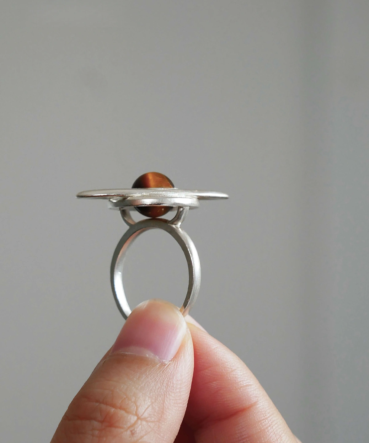 Hand holding Lazesoul’s handmade Saturn Ring in 925 sterling silver, featuring a polished tiger’s eye gemstone as Saturn with sculptural orbit bands; celestial-inspired artisan jewelry blending cosmic symbolism with modern elegance.