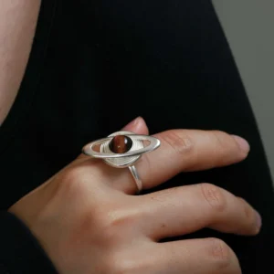 Close-up of a hand wearing Lazesoul’s handmade Saturn Ring in 925 sterling silver, featuring a dark tiger’s eye gemstone as Saturn with silver orbit bands; celestial-inspired artisan jewelry with cosmic elegance.