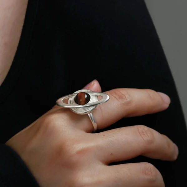 925 Sterling Silver Tiger’s Eye Saturn Ring 02 Close-up of a hand wearing Lazesoul’s handmade Saturn Ring in 925 sterling silver, featuring a dark tiger’s eye gemstone as Saturn with silver orbit bands; celestial-inspired artisan jewelry with cosmic elegance.