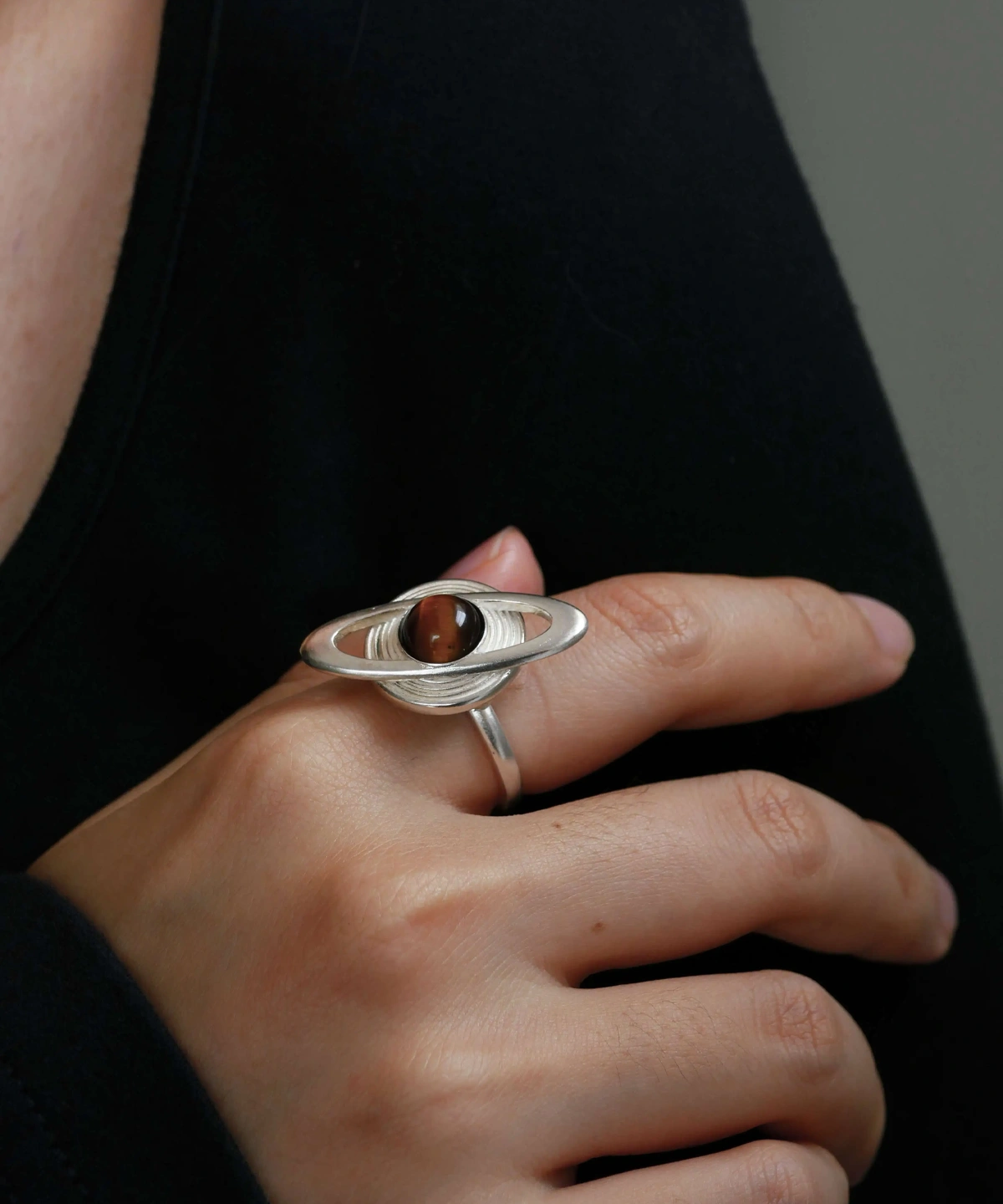 Close-up of a hand wearing Lazesoul’s handmade Saturn Ring in 925 sterling silver, featuring a dark tiger’s eye gemstone as Saturn with silver orbit bands; celestial-inspired artisan jewelry with cosmic elegance.