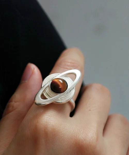 Hand wearing Lazesoul’s handmade Saturn Ring in 925 sterling silver, featuring a sculptural tiger’s eye gemstone as Saturn with orbit-inspired rings; artisanal celestial jewelry with modern elegance.