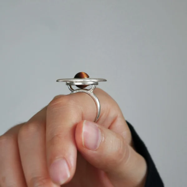Close-up of a hand wearing Lazesoul’s handmade Saturn Ring in 925 sterling silver, featuring a polished tiger’s eye gemstone as Saturn with orbit-inspired bands; celestial artisan jewelry blending cosmic symbolism with timeless elegance.