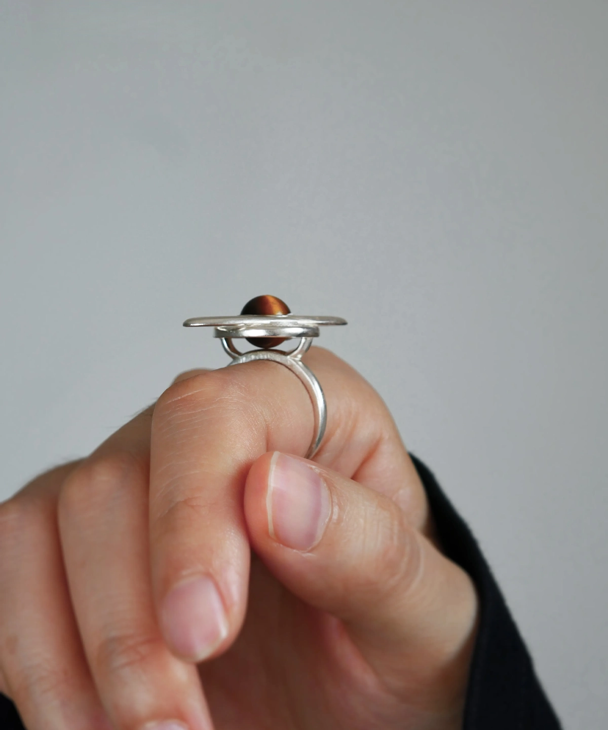 Close-up of a hand wearing Lazesoul’s handmade Saturn Ring in 925 sterling silver, featuring a polished tiger’s eye gemstone as Saturn with orbit-inspired bands; celestial artisan jewelry blending cosmic symbolism with timeless elegance.