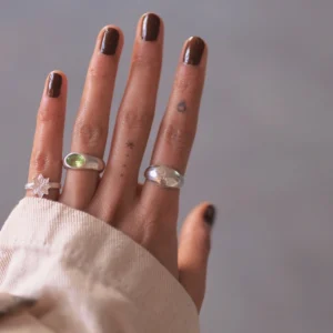 Hand with brown nails wearing silver rings, including an April Birthstone Ring with lab grown diamond, styled with leaf and star motifs, tattoos, and a soft sleeve.