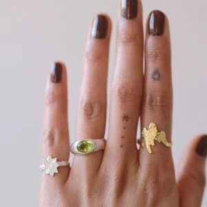 Close-up of a hand wearing two Silver Rings with natural peridot gemstones and a gold angel-shaped ring; elegant August Birthstone Ring styling with sculptural bands, vibrant green stones, and minimalist tattoos, showcasing handcrafted Natural Peridot Ring artistry.