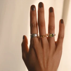 Close-up of a hand wearing two Silver Rings with natural peridot gemstones and a gold accent ring; elegant August Birthstone Ring styling with sculptural bands and vibrant green stones, highlighting handcrafted Natural Peridot Ring artistry.