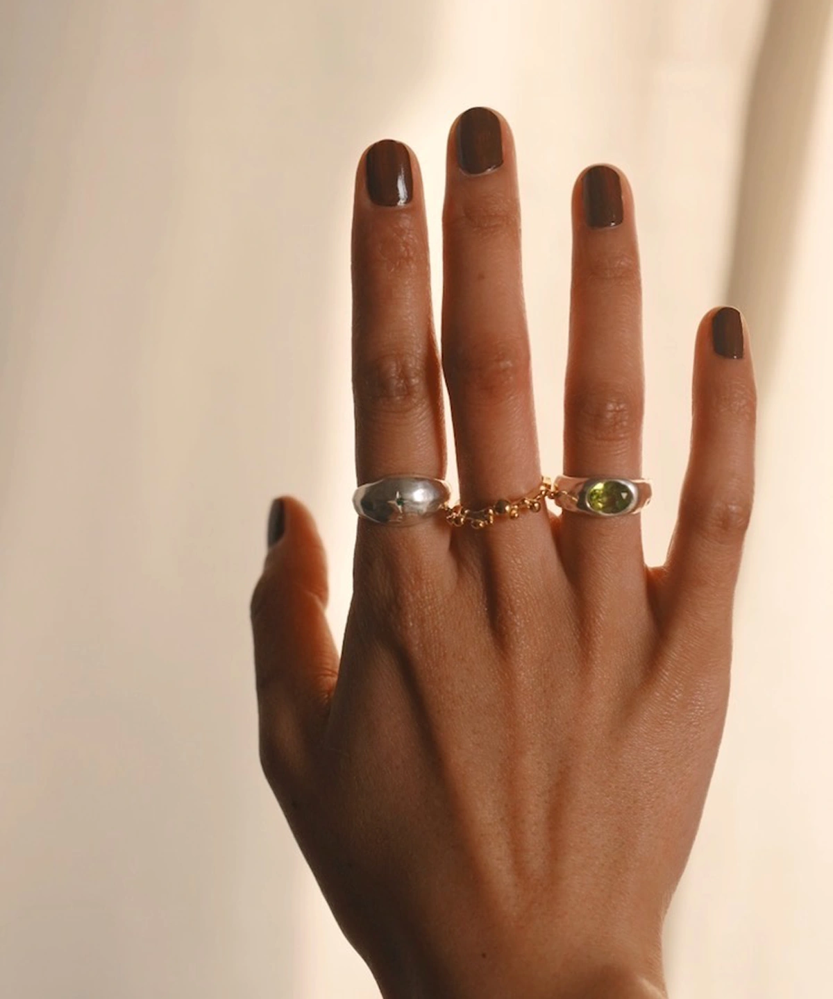 Close-up of a hand wearing two Silver Rings with natural peridot gemstones and a gold accent ring; elegant August Birthstone Ring styling with sculptural bands and vibrant green stones, highlighting handcrafted Natural Peridot Ring artistry.