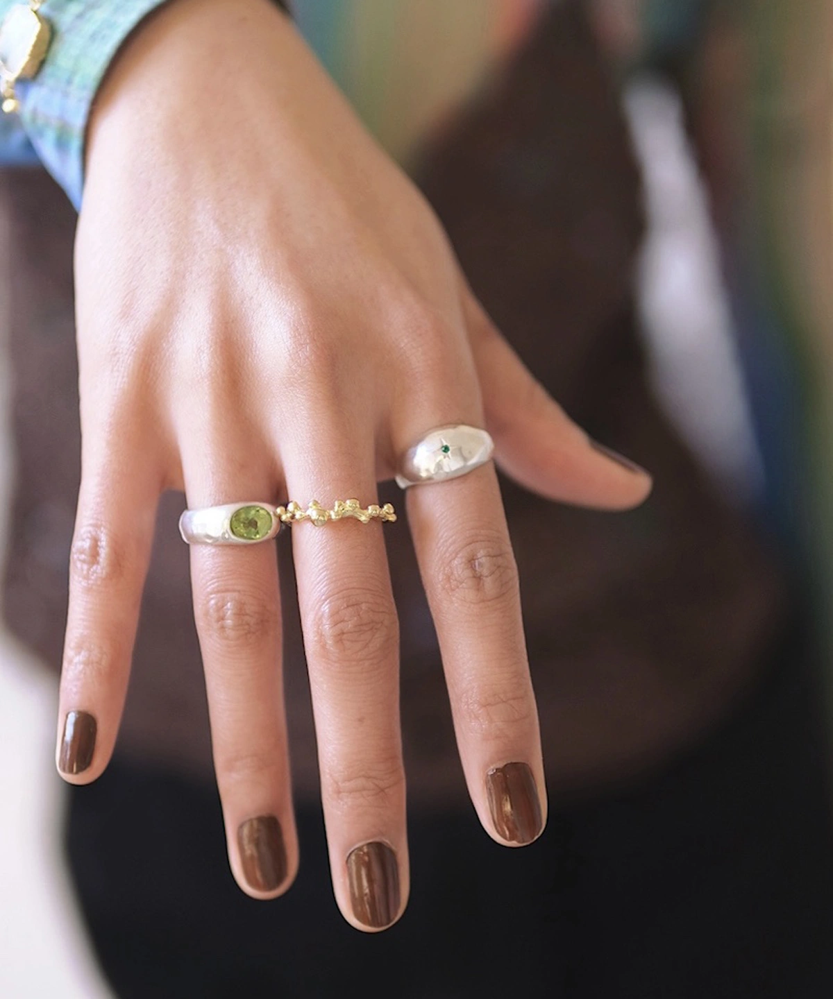Close-up of a hand wearing two Silver Rings with natural peridot gemstones and a gold accent ring; elegant August Birthstone Ring designs with sculptural bands and vibrant green stones, showcasing handcrafted Natural Peridot Ring artistry.