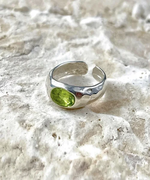 Sterling Silver Ring with oval-shaped natural peridot gemstone displayed on textured stone; elegant August Birthstone Ring design with open-ended band and handcrafted Silver Ring texture, showcasing vibrant green hues and artisanal detail.