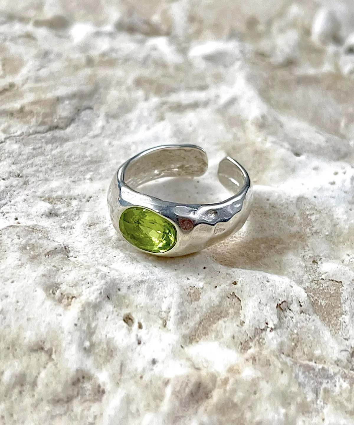 Sterling Silver Ring with oval-shaped natural peridot gemstone displayed on textured stone; elegant August Birthstone Ring design with open-ended band and handcrafted Silver Ring texture, showcasing vibrant green hues and artisanal detail.