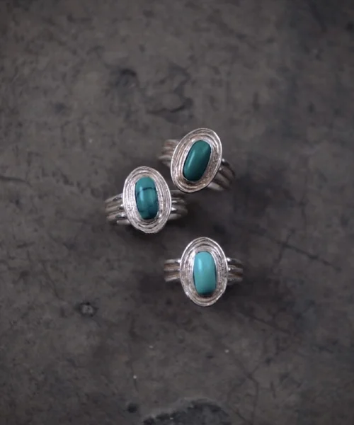 Three sterling silver December Birthstone Rings with natural turquoise stones arranged on a dark textured surface, showcasing handcrafted bezel settings and multi-band shanks.
