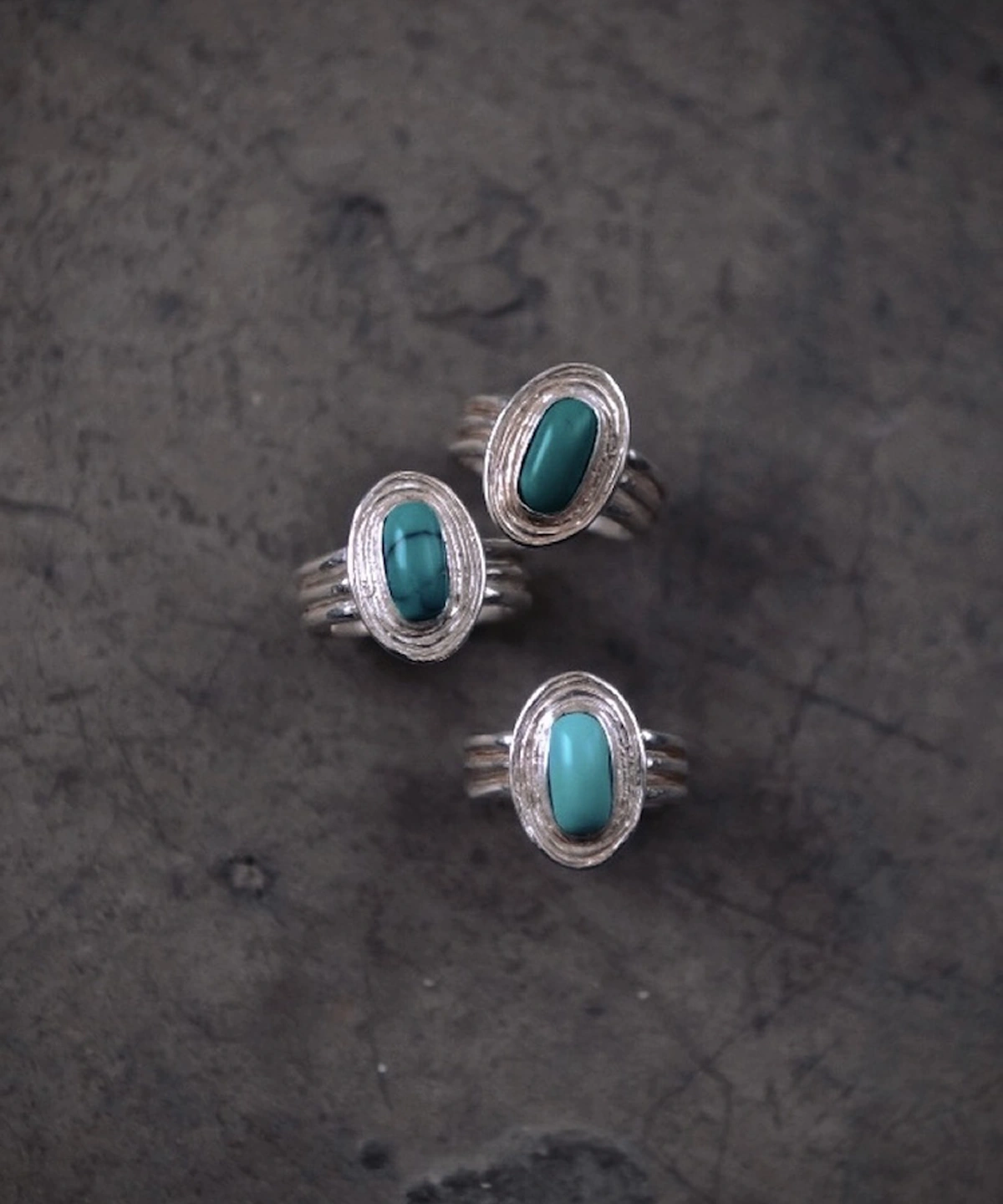 Three sterling silver December Birthstone Rings with natural turquoise stones arranged on a dark textured surface, showcasing handcrafted bezel settings and multi-band shanks.
