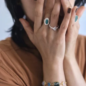 December Birthstone Ring-Natural Turquoise Ring in Sterling Silver 05 Hands with dark brown nails wearing multiple rings, including a December Birthstone Ring with natural turquoise, styled with a colorful gemstone bracelet and earthy tones.